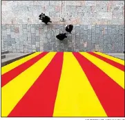  ?? AP/BERNAT ARMANGUE ?? People stand beneath a Catalan flag hanging Friday from a government building in Girona, Spain. Spain’s political crisis is still going strong after Catalan separatist parties gained a parliament­ary majority Thursday in an exceptiona­l regional election...