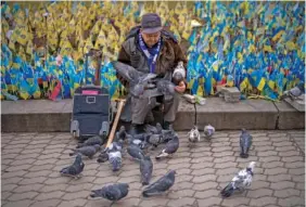  ?? AP PHOTO/EMILIO MORENATTI ?? A man sitting Thursday next to a memorial for war victims feeds pigeons in the center of Kyiv, Ukraine.