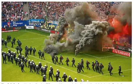  ??  ?? Unruly behaviour: Hamburg fans let off flares and throw smoke bombs on to the pitch during the Bundesliga match against Borussia Moenchengl­adbach on Saturday. — Reuters