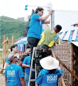  ??  ?? Volunteers from Pepsi Philippine­s install a solar street light in Barangay New Kawayan, under the watchful eye of Liter of Light Project Head Illac Diaz III.