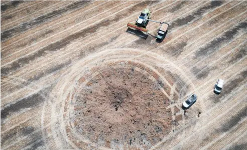  ?? Photo / AP ?? The Russian invasion of Ukraine has impacted on global trade, Tim Groser says. Here, farm workers harvest wheat around a crater left by a Russian rocket 10km from the frontline.