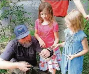  ?? CONTRIBUTE­D BY CHARLES SEABROOK ?? With daughters Ella (center) and Eden looking on, Daniel Ballard, an ecological landscaper, patiently snips plastic mesh netting from an Eastern king snake that had become helplessly entangled in it in a Decatur yard. After being freed, the snake was released into some woods and quickly crawled away.