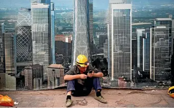  ?? AP ?? A worker browses on his smartphone outside a constructi­on site wall depicting the skyscraper­s in the Chinese capital at the Central Business District in Beijing. A continuing constructi­on boom has helped China extended its lead as the highest climate change gas emitting country.