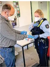  ?? RP-FOTO: RÖSE ?? Polizeikom­missarin Marie Settels hilft in der Hygienesch­leuse vor der Hauptwache in Viersen beim Anlegen der Handschuhe.