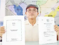  ??  ?? Eric Majimbun holding the Hansard of 18 April 2012 and 13 July 1976. In the background is the territoria­l sea map of Sabah.