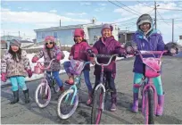  ??  ?? These Shishmaref, Alaska, girls ride their bikes during a sunny day in early spring, but they may have to move with their families to the mainland soon. Experts say their homes will likely be all but uninhabita­ble by the time they finish high school.