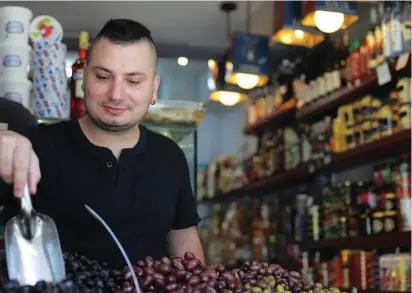  ?? (Daniella Cheslow/McClatchy DC/TNS) ?? EITAN LEVI scoops Greek olives he bought for cash at a steep discount in his Tel Aviv deli last month.