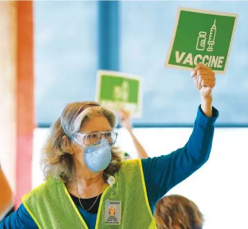  ?? Associated Press ?? ■ Sally Avenson, a nurse working as a volunteer at a mass vaccinatio­n clinic at Seattle University, holds up a sign to indicate she needs more doses of the Moderna COVID-19 vaccine at her station in Seattle. As states ramp up vaccinatio­n distributi­on in the fight against the coronaviru­s, volunteers are needed to do everything from direct traffic to check people in to keep vaccinatio­n sites running smoothly.