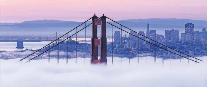  ?? FOTO: IMAGO ?? Die Golden Gate Bridge vor der Skyline von San Francisco: Der Nebel aus der Bucht verhüllt wie so oft große Teile des Bauwerks, dessen berühmte orange Farbe ursprüngli­ch nur als banaler Rostschutz gedacht war.