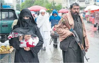  ?? EBRAHIM NOROOZI THE ASSOCIATED PRESS ?? An Afghan woman walks through a market in downtown Kabul on May 3 as a Taliban fighter stands guard.