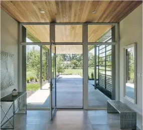  ??  ?? The Rideau River can be seen through the huge glass door at the front of the home. Rich oak wood extends from the ceiling of the front porch into the entrance of the house.