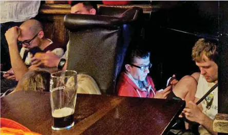  ??  ?? Agonising wait: Pub-goers check their phones as they crouch on the floor or use tables for cover