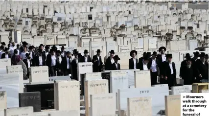  ?? Oded Balilty ?? > Mourners walk through at a cemetery for the funeral of Menahem Zachach, 24, who died during Lag BaOmer celebratio­ns at Mt Meron in northern Israel. Left, security officials and rescuers stand around the bodies of victims of the stampede at a religious festival