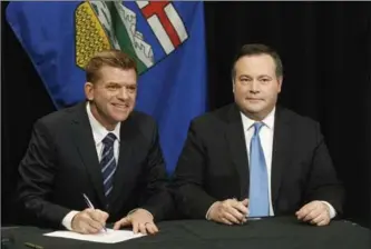  ?? JASON FRANSON, THE CANADIAN PRESS ?? Alberta Wildrose Leader Brian Jean, left, and Alberta PC Leader Jason Kenney sign a unity deal between the two parties in Edmonton on Thursday. The merger has to be approved by members of both parties.