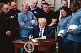  ?? Andrew Harrer / Bloomberg ?? With steel and aluminum workers gathered around on Thursday, President Donald Trump signs the proclamati­on on tariffs in the White House’s Roosevelt Room.