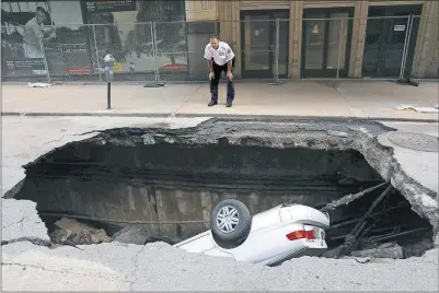  ?? [CHRISTIAN GOODEN/ST. LOUIS POST-DISPATCH] ?? A St. Louis police officer looks over a large hole in 6th Street between Olive and Locust streets in St. Louis that swallowed a Toyota Camry on Thursday. It isn’t immediatel­y clear what caused the collapse.