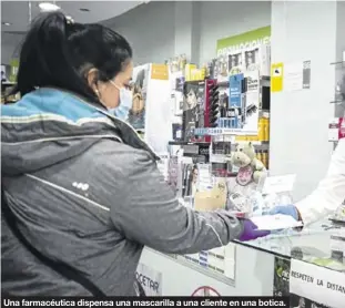  ??  ?? Una farmacéuti­ca dispensa una mascarilla a una cliente en una botica.