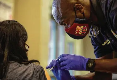  ?? Marie D. De Jesús / Staff photograph­er ?? Houston Fire Department Capt. Charles Harper inoculates a woman with Pfizer’s COVID-19 vaccine at Hollibrook Elementary School. The positivity rate for COVID-19 cases in Harris County reached 20.4 percent last week.