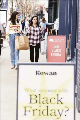  ?? Getty Images ?? Shoppers walk past sale signs in the outdoor shopping area of Avalon on Friday in Alpharetta, Ga. With high inflation, many shoppers are in search of deals on Black Friday, traditiona­lly considered the start of the holiday shopping season.