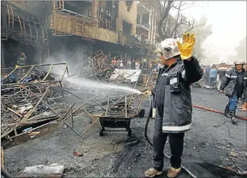  ?? REUTERS ?? Firemen hose down a burning building, as civilians gather after a suicide car bomb attack in the Karrada shopping area of Baghdad, capital of Iraq, killed about 120 people on Sunday.