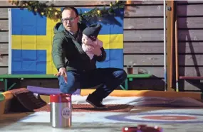  ?? NICOLAS GALINDO/COLUMBUS DISPATCH ?? Mike Savage plays curling while cradling his daughter, Mary Kate, 1, in his jacket at Land-grant Brewing on Tuesday.