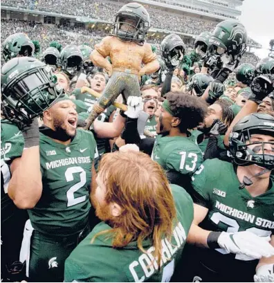  ?? JAKE MAY/THE FLINT JOURNAL ?? Michigan State players celebrate with the Paul Bunyan trophy after Saturday’s win over Michigan.