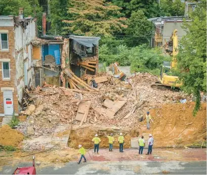  ?? BALTIMORE SUN JERRY JACKSON/ ?? Workers stand next to a sinkhole in the 700 block of East North Avenue last month as threatened homes are demolished.