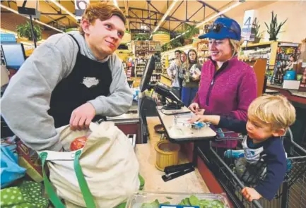  ?? Paul Aiken, Daily Camera ?? Evan Kamlet, a checker at Alfalfa’s Market, 1651 Broadway in Boulder, searches for Joy Larkin’s keys in her grocery bag as her 2-year-old son, Trey, looks on. The keys were accidental­ly covered with groceries during checkout.