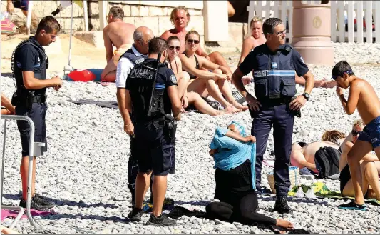  ??  ?? Police force a woman to take off her outer clothing on the beach in Nice near the Promenade des Anglais on Tuesday. The woman did not appear to have been wearing a burkini, which has been banned on beaches by some local mayors.