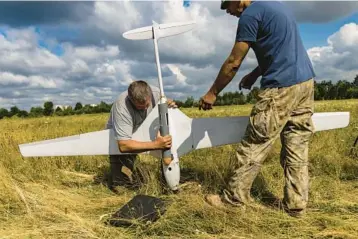  ?? DAVID GUTTENFELD­ER/THE NEW YORK TIMES ?? Ukrainian troops practice attaching a dummy bomb to the undercarri­age of a Punisher, a high-end fixed-wing military drone manufactur­ed in Ukraine, on July 25 in an open field on the outskirts of Kyiv.