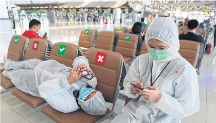  ?? SOMCHAI POOMLARD ?? Two people in full protective outfits fiddle with their phones as they wait to catch flights out of Suvarnabhu­mi airport yesterday. Many provinces have imposed travel restrictio­ns in the wake of the fresh Covid-19 outbreak.