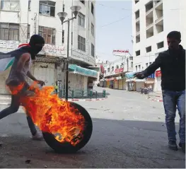  ?? (Mussa Qawasma/Reuters) ?? A PALESTINIA­N pushes a burning tire during clashes with Israeli troops in Hebron yesterday, following a protest in support of security prisoners on hunger strike.