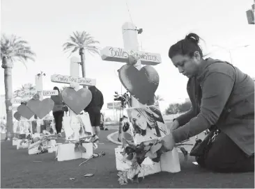  ??  ?? Cece Navarrette places flowers at a cross for her cousin, Bailey Schweitzer, who was among those killed during the mass shooting in Las Vegas. Crosses were erected beside the Welcome to Las Vegas sign.