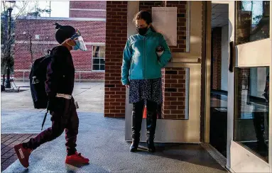  ?? PHOTOS BY ALYSSA POINTER/ALYSSA.POINTER@AJC.COM ?? John Robert Lewis Elementary School music teacher Elena Prestwood welcomes a student wearing a face shield and face mask into the school building Tuesday.