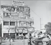  ?? RICHARD HARRINGTON/THREE LIONS/GETTY IMAGES ?? A man buys fruit in front of a hoarding promoting several films in Delhi in 1950.