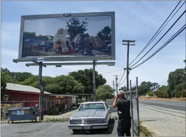  ?? PHOTOS BY JENNIE BLEVINS — MERCURY-REGISTER ?? Photograph­er Thomas Broening snaps a photo of his billboard in Oroville, that depicts a homeless encampment with a huge teddy bear resting on a shopping cart.
