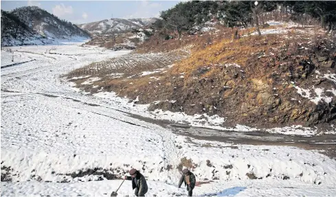  ??  ?? HIDDEN LEGACY: Villagers Song Hong-ik, left, and Kim Ri-jun carry shovels as they walk past Ryongyon-ri hill, where remains of soldiers they claim fought in the Korean War are buried.