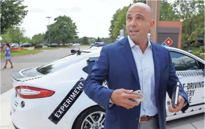  ?? PHOTOS BY ELAINE CROMIE, SPECIAL TO THE DETROIT FREE PRESS, VIA USA TODAY NETWORK ?? Domino’s Chief Developmen­t Officer Kelly Garcia stands next to the Ford Fusion self-driving hybrid that will be used as a test pizza delivery vehicle in Ann Arbor, Mich.