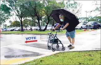  ?? Lynne Sladky / Associated Press ?? Franklin Castellon, 76, shields himself from the rain as he walks to an early voting site on Monday in Miami. Florida begins in-person early voting Monday in much of the state as the Trump campaign tries to cut into an early advantage Democrats have posted in mail-in votes in the key swing state.