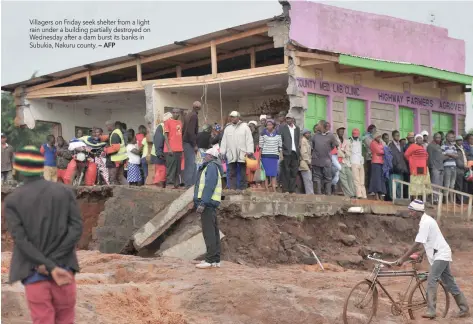  ?? — AFP ?? Villagers on Friday seek shelter from a light rain under a building partially destroyed on Wednesday after a dam burst its banks in Subukia, Nakuru county.
