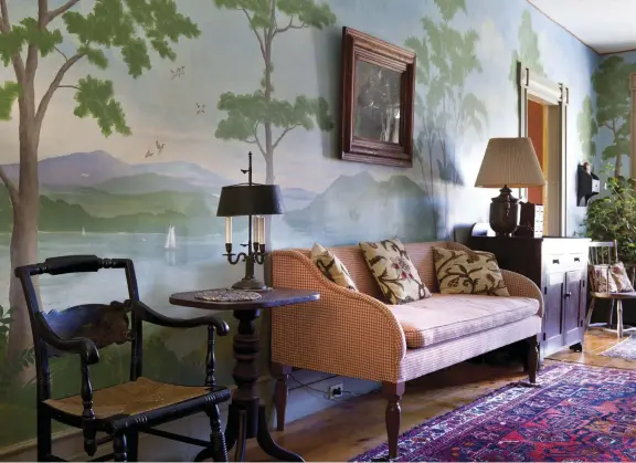  ??  ?? ABOVE A sweeping, hand-painted mural of a Hudson River scene is painted on the wall of the entrance hall, which is wide enough to provide seating on a gingham-covered sofa.