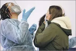 ?? Mario Tama Getty Images ?? MERLINE JIMENEZ, left, gives a person a bit of direction before administer­ing a COVID-19 nasal swab on Tuesday at a testing site at LAX.