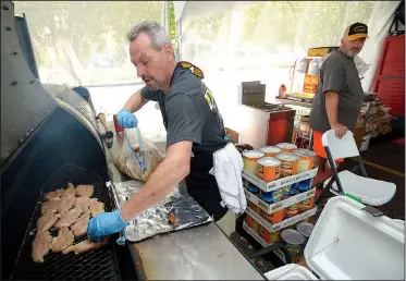  ?? NWA Democrat-Gazette/ANDY SHUPE ?? Randy Adams (left) places marinaded chicken breasts on the smoker Friday in the official barbecue tent during the annual Bikes, Blues & BBQ Motorcycle Rally in Fayettevil­le. Organizers put their interest in tailgating and making food for others to use...