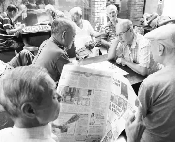  ?? — Reuters photo ?? A man reads a newspaper as others play checkers in Singapore.