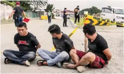  ??  ?? TAGUIG CLASH – Three policemen who are members of the kidnap gang are tied up as police officers sift through the scene of the shootout in Tandem St. Taguig City, Tuesday. (Jun Arañas)