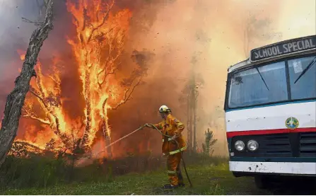  ??  ?? Fighting the flames: A New South Wales Rural Fire Service firefighte­r spraying water on a bushfire next to a school bus in the Salt Ash suburb, located north of Newcastle, Australia. — AFP