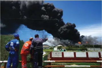  ?? The Associated Press ?? Workers of the Cuba Oil Union, known by the Spanish acronym CUPET, watch a huge rising plume of smoke from the Matanzas Supertanke­r Base, as firefighte­rs work to quell a blaze which began during a thundersto­rm the night before, in Matazanas, Cuba, on Saturday. Cuban authoritie­s say lightning struck a crude oil storage tank at the base, causing a fire that led to four explosions which injured more than 50 people.