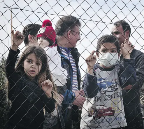  ?? LOUISA GOULIAMAKI / AFP / GETTY IMAGES ?? Migrants stand behind a fence at the Hellinikon camp in Athens on Monday, in protest of poor living conditions.