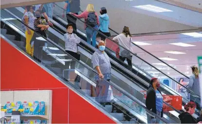  ?? NELVIN C. CEPEDA U-T ?? Shoppers take the escalator between the first and second levels of the Target in Mission Valley on Friday. Though some still went to stores in person, Adobe Analytics forecast that online spending on Black Friday would be up 20 percent from 2019.