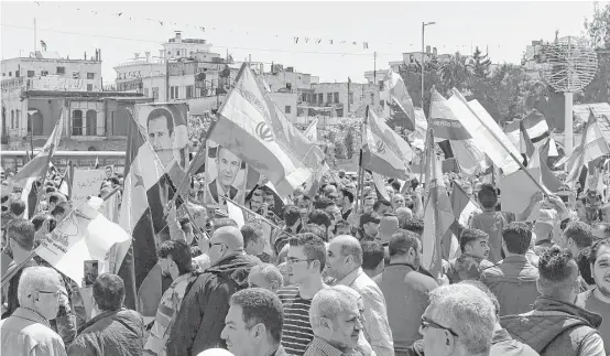  ?? GEORGE OURFALIAN / AFP / Getty Images ?? Syrians wave the Syrian and Iranian flags and portraits of President Bashar al-Assad as they gather in Aleppo's Saadallah al-Jabiri square Saturday to condemn the airstrikes carried out by the United States, Britain and France against the Syrian regime.